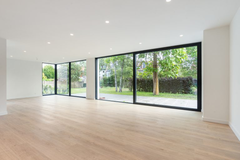 Grote moderne woonkamer met grote raampartijen en uitzicht op tuin, veel licht en ruimte.
